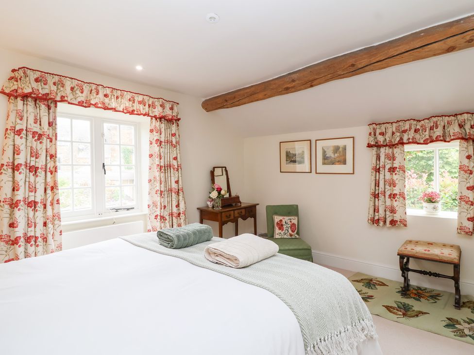 A bedroom with a bed and a chair at Magdalen Cottage in Hook Norton