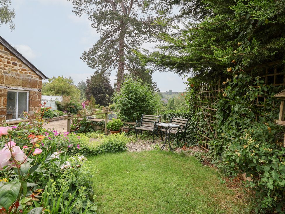 A garden with flowers, benches and a table at Magdalen Cottage in Hook Norton