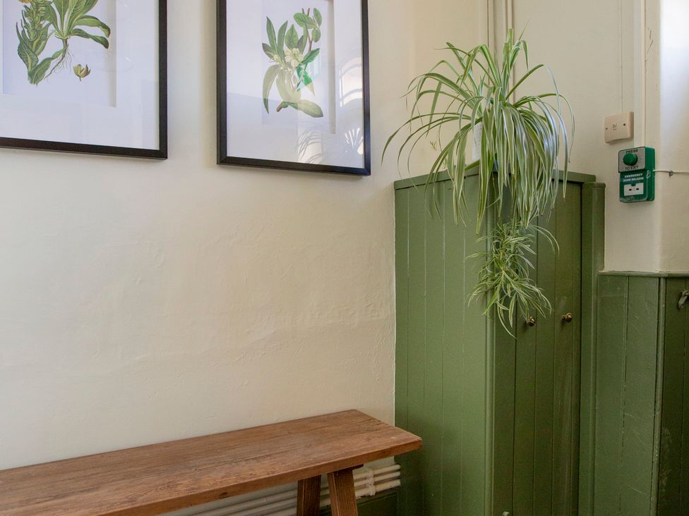 An entrance with a wooden bench and framed plant artwork at Apartment 1, 86 Dyer Street Cirencester
