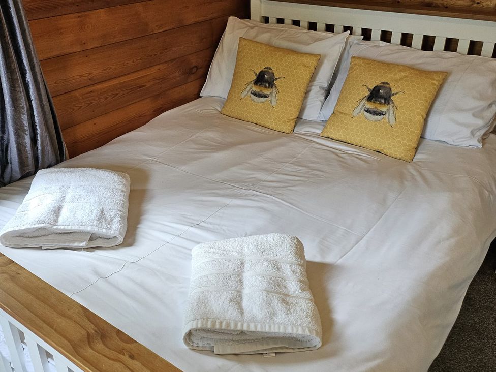 A bedroom with a double bed and bee patterned pillows at Swn Yr Afon - No 333 near Trawsfynydd