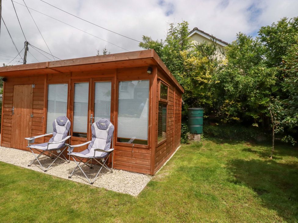 A wooden cabin with chairs outside in the garden at Heatherlea Cottage St. Austell