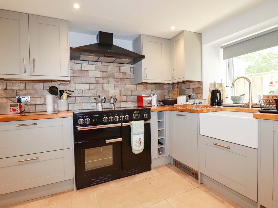 A kitchen with cabinets, stove, sink, and utensils at Heatherlea Cottage in St. Austell