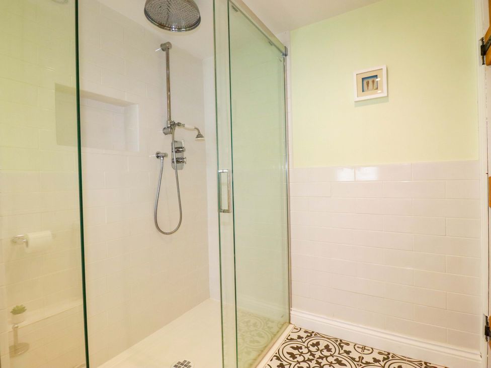 A shower with glass door and wall tiles at Heatherlea Cottage in St. Austell