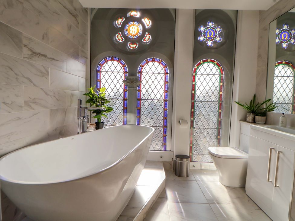 A bathroom with a bathtub, toilet, and stained glass windows at 1 Chapel Place Chester