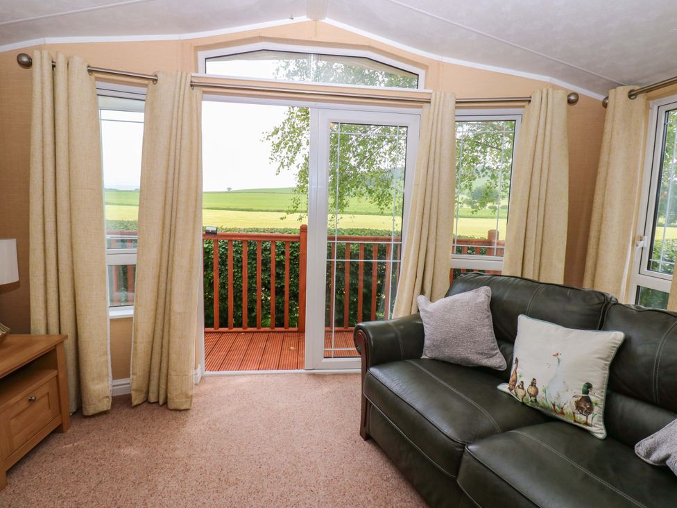 A snug with a sofa and open doors leading to a deck at Plot 12 in Carlisle