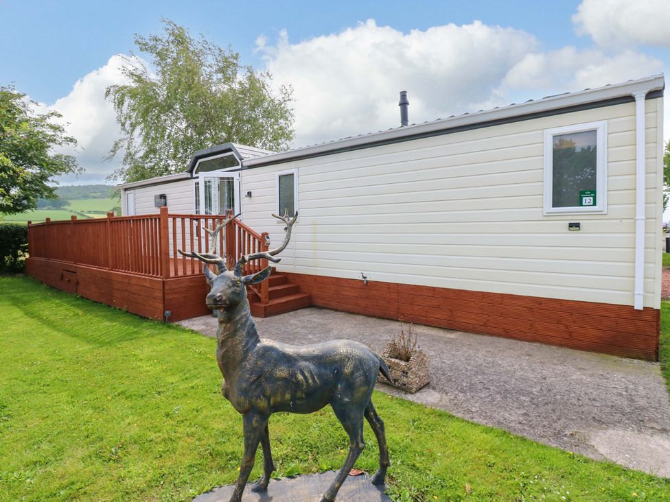 A mobile home with decking and a deer statue at Plot 12 in Carlisle