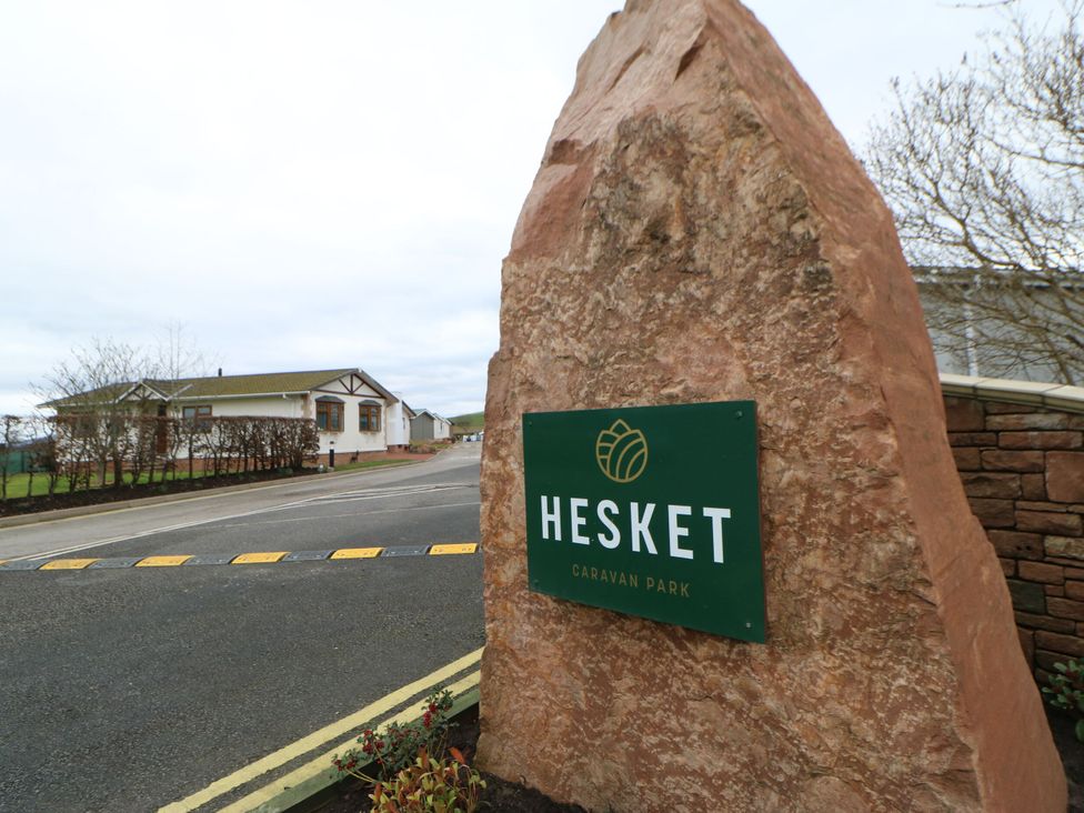A sign for Hesket Caravan Park with buildings and pathway at Hesket Caravan Park in Carlisle