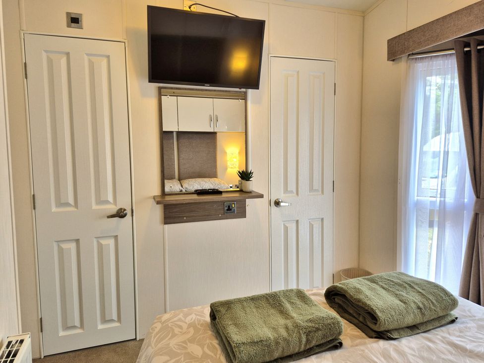 A bedroom with a television and towels on a bed at Fernwood Lodge in Fritton near Belton, Norfolk