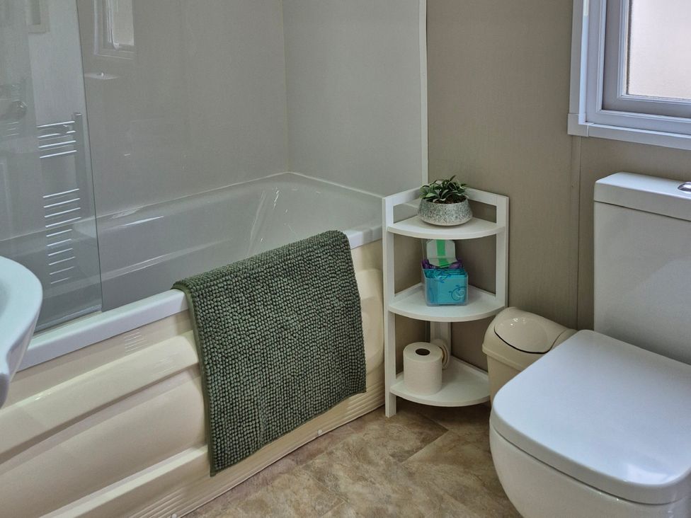 A bathroom featuring a bathtub, toilet, and shelf with toiletries at Fernwood Lodge in Fritton near Belton, Norfolk