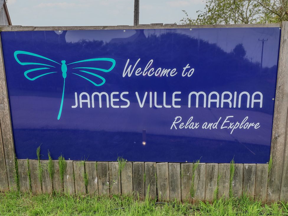 A sign welcoming visitors to James Ville Marina with a dragonfly design in Brigg