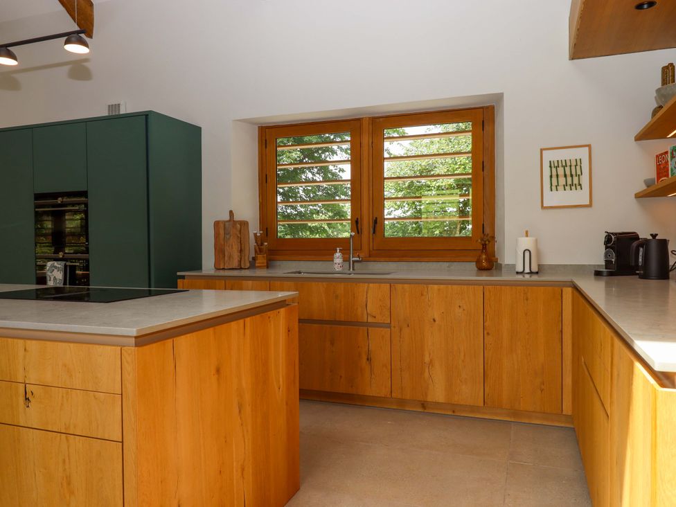 A kitchen with wooden cabinets and a window at Lower Walreddon Barn Tavistock
