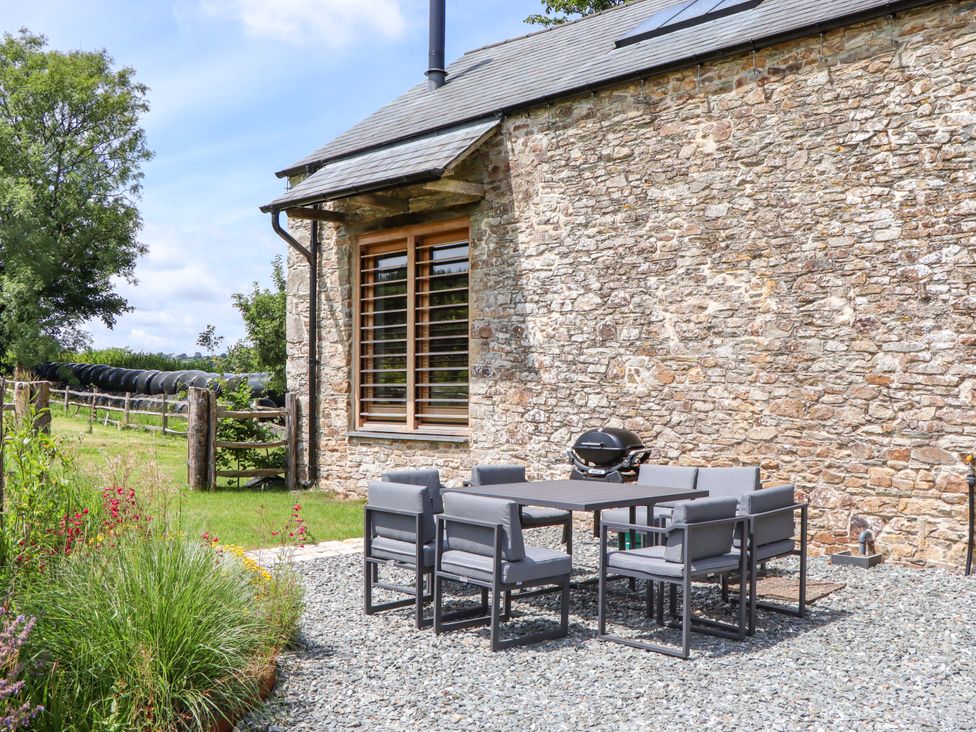 An outdoor area with a table and chairs near a stone wall at Lower Walreddon Barn Tavistock