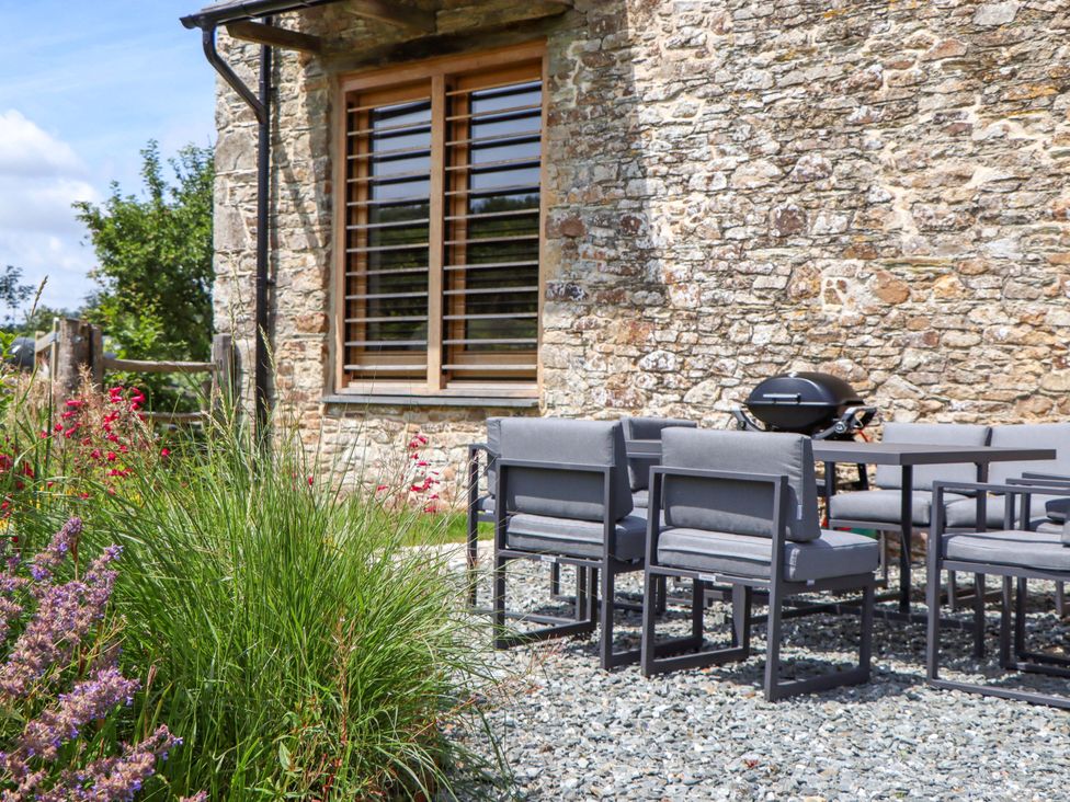 A patio area with a stone wall, seating, table, and grill at Lower Walreddon Barn Tavistock