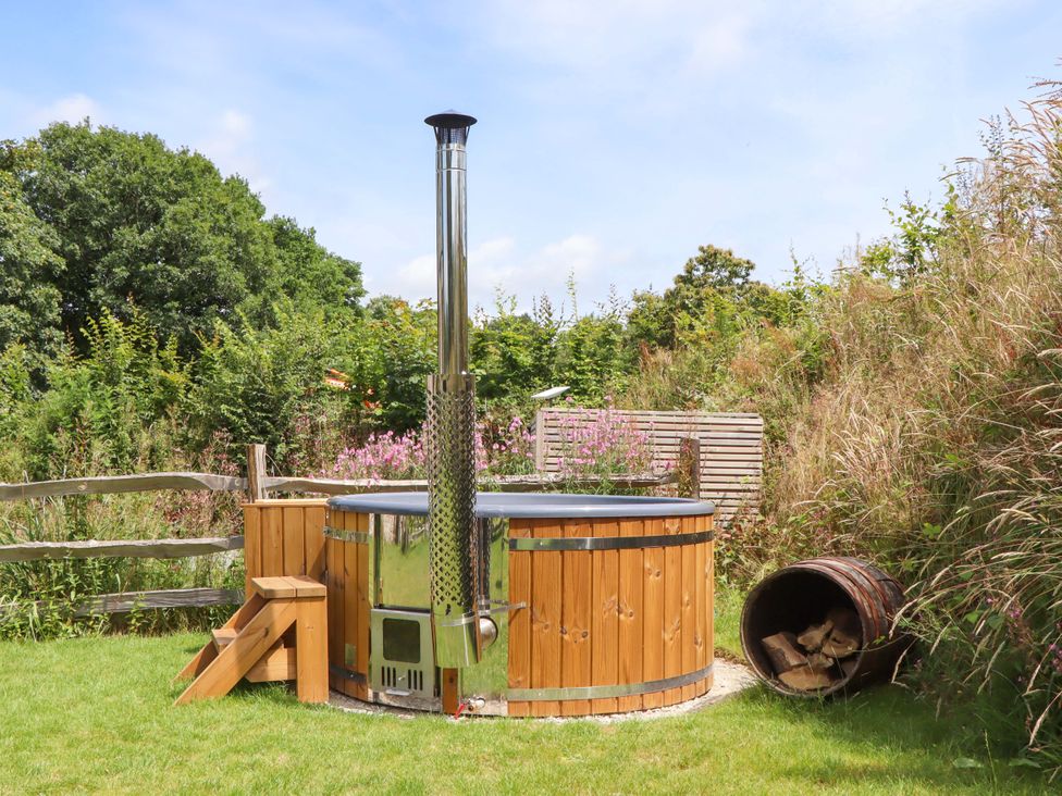 A hot tub with wooden surround and chimney in a garden at Lower Walreddon Barn Tavistock
