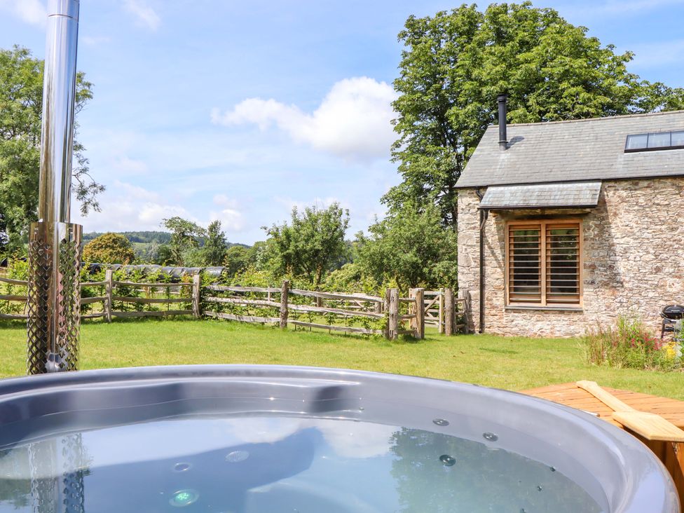 A hot tub with a house and fence in the background at Lower Walreddon Barn Tavistock