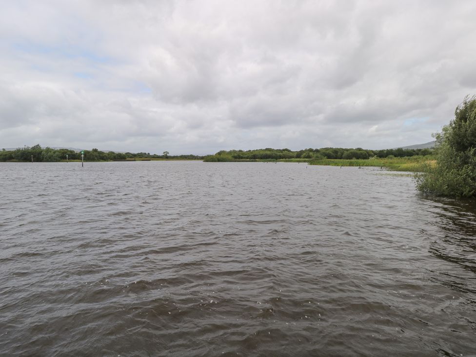 A body of water with surrounding greenery and cloudy sky at The Cottage in Ballinagleira