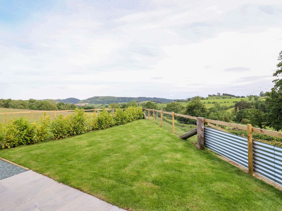 A garden with a lawn and fence overlooking hills at Charollais in Oswestry