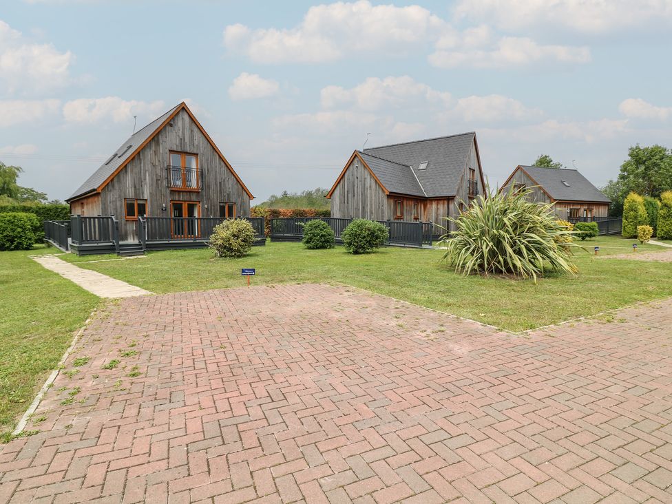 Three wooden houses with a pathway and lawn at Lodge 13 in Brigg