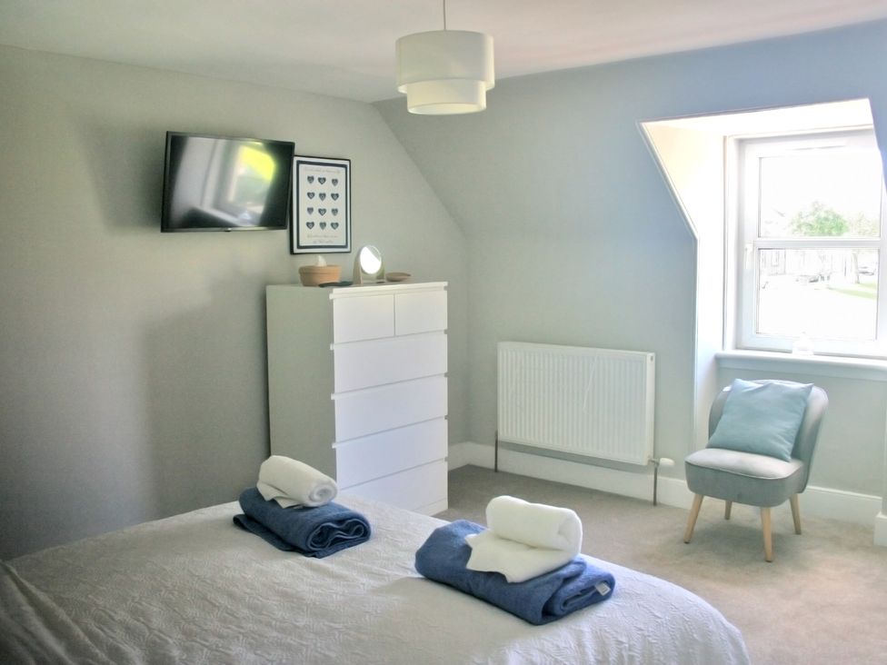 A bedroom with a television and towels on a bed at 2 Links Place in Nairn