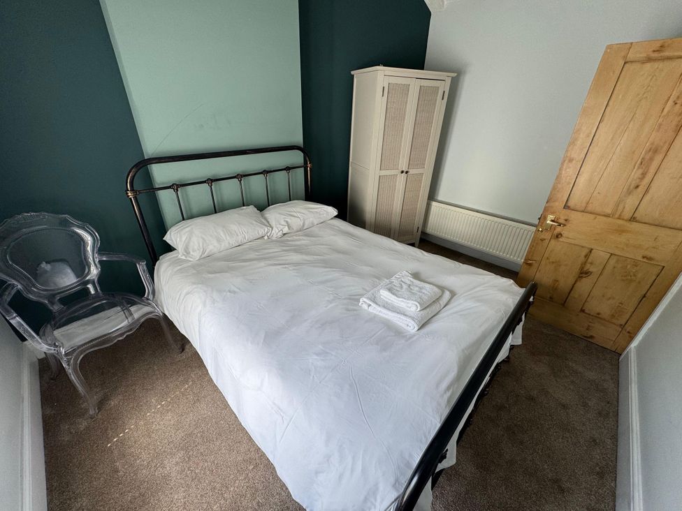 A bedroom with a bed, wardrobe, clear chair and door at 18 The Wharfage in Ironbridge
