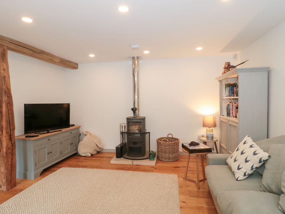 A living room with a television and wood burner stove at The Threshing Barn in Chipping Norton