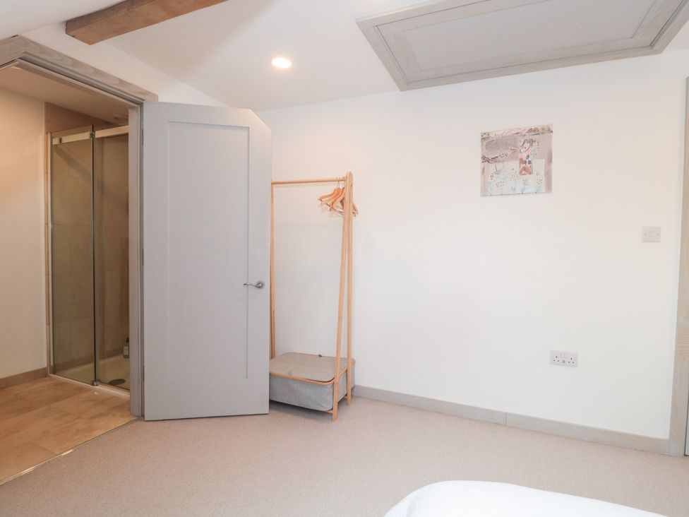 A bedroom with a shower door and clothes rack at The Threshing Barn in Chipping Norton
