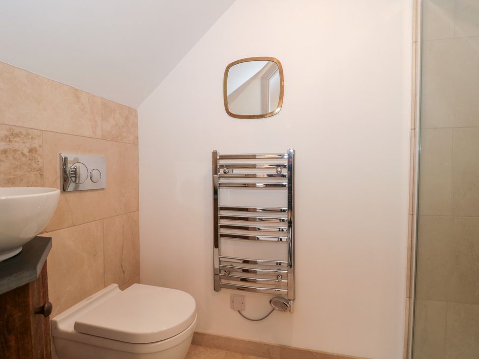A bathroom with a toilet, hand basin, towel radiator and a mirror at The Threshing Barn Chipping Norton