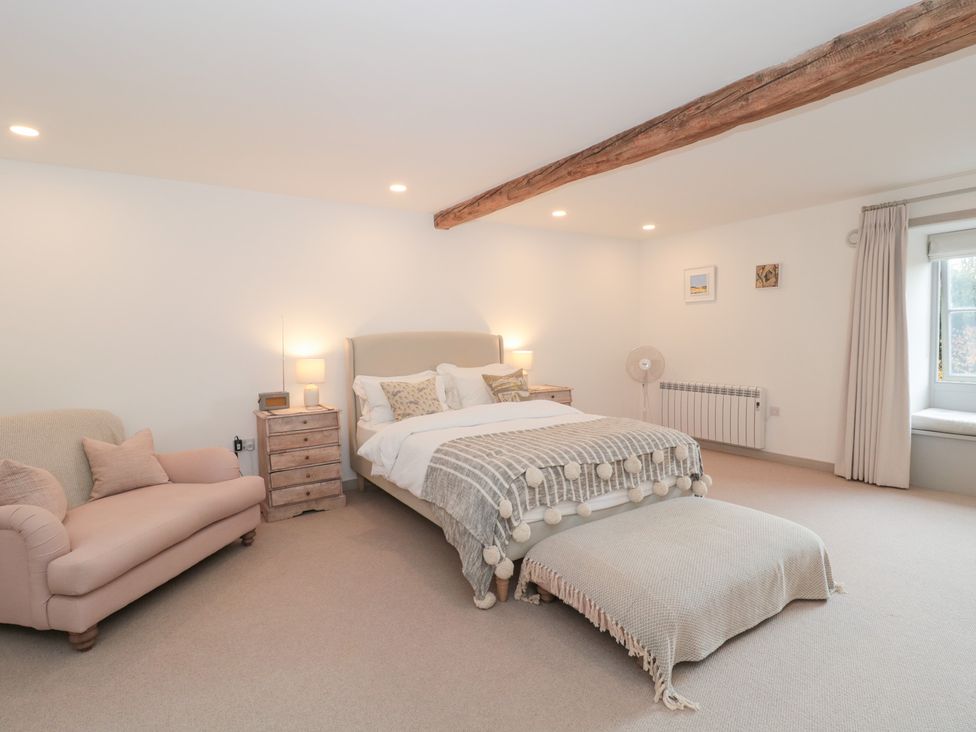 A bedroom with a bed, nightstand, sofa, and window at The Threshing Barn in Chipping Norton