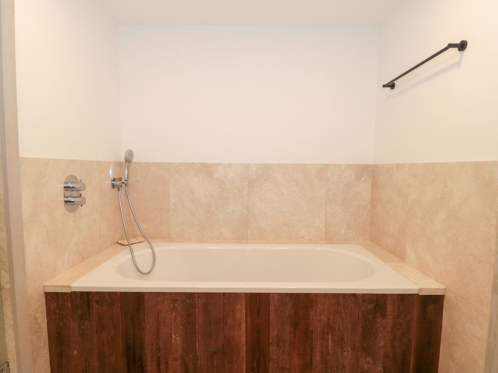 A bathtub with a showerhead in a bathroom at The Threshing Barn in Chipping Norton