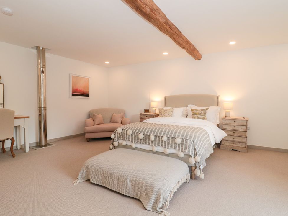 A bedroom with a bed, sofa, desk, and chair at The Threshing Barn in Chipping Norton