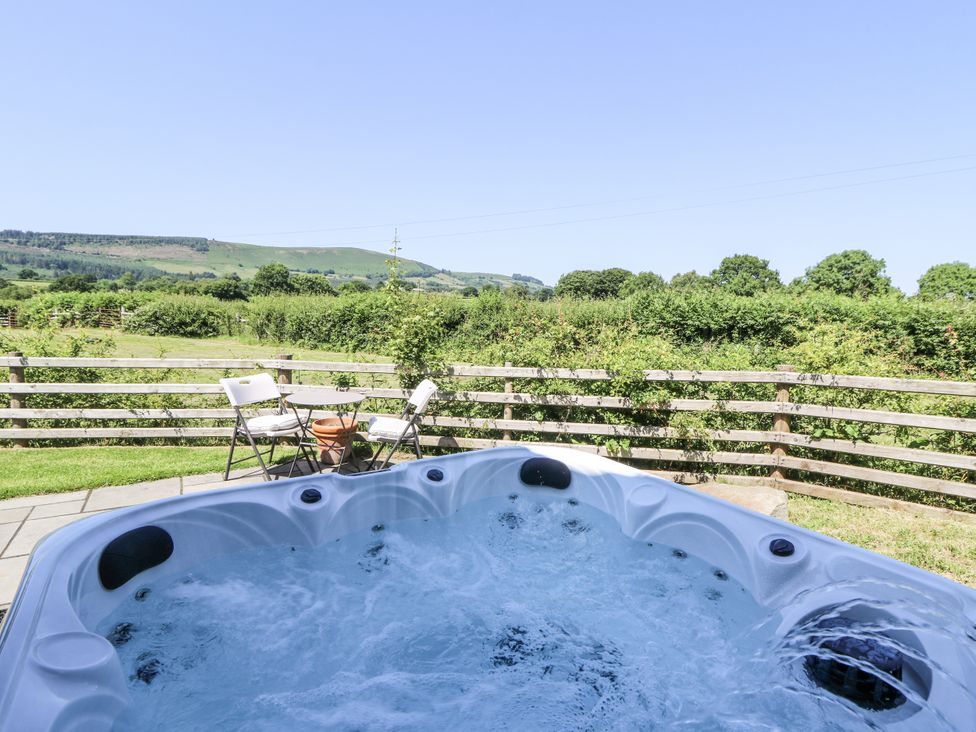 A hot tub with chairs and a table in a garden area at Little Penrhosgoch Barn in Llandrindod Wells