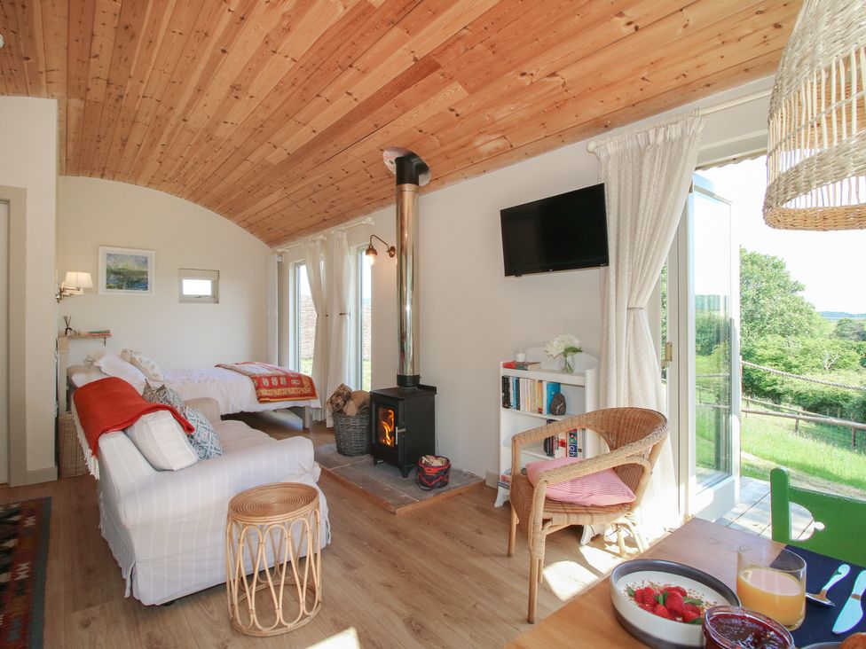 A living room with a sofa, bed, and fireplace at Squirrel's Drey in Chapel Lawn near Clun