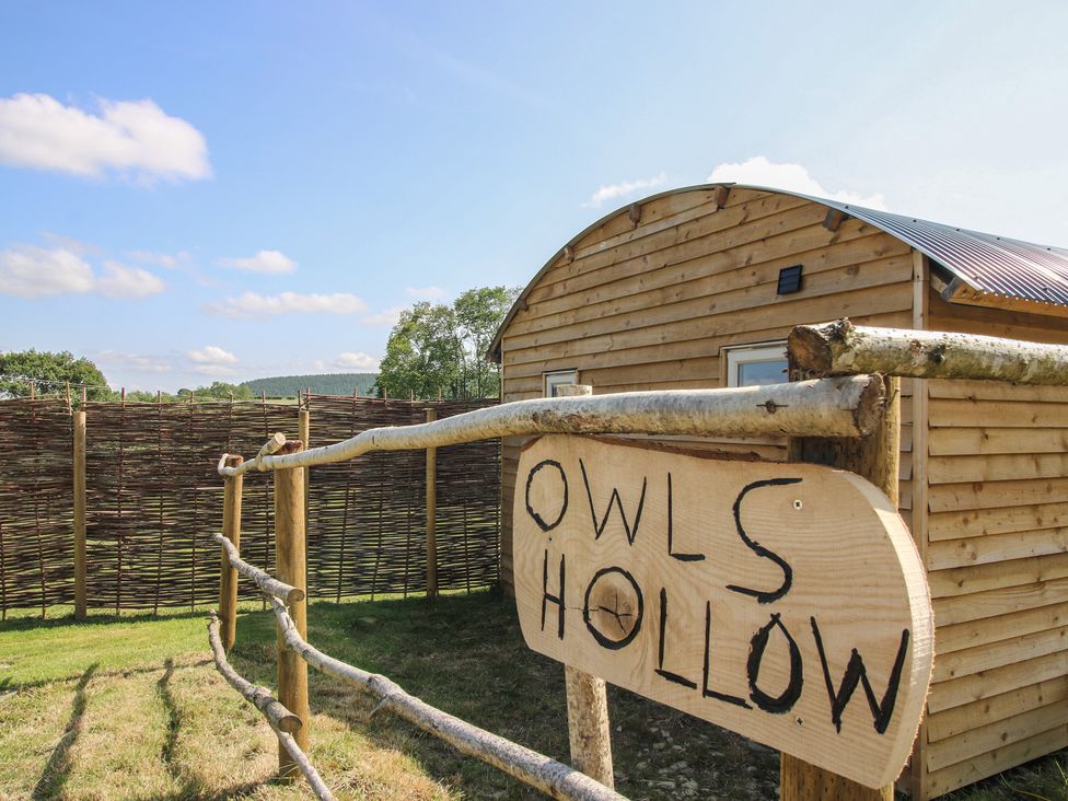 A wooden sign in front of a cabin at Owl's Hollow in Chapel Lawn near Clun