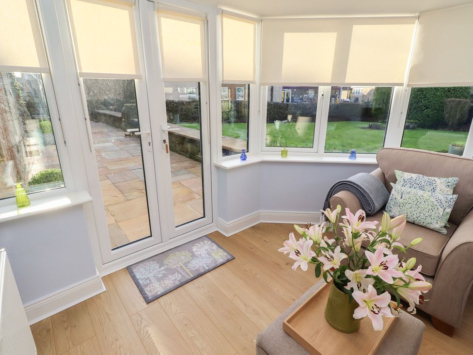 A conservatory with a sofa and flowers at Linn Cottage in Hexham