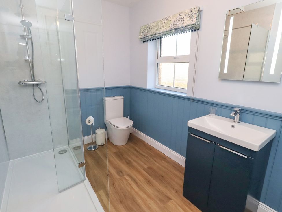 A bathroom with a shower, toilet, sink, and window at Linn Cottage in Hexham