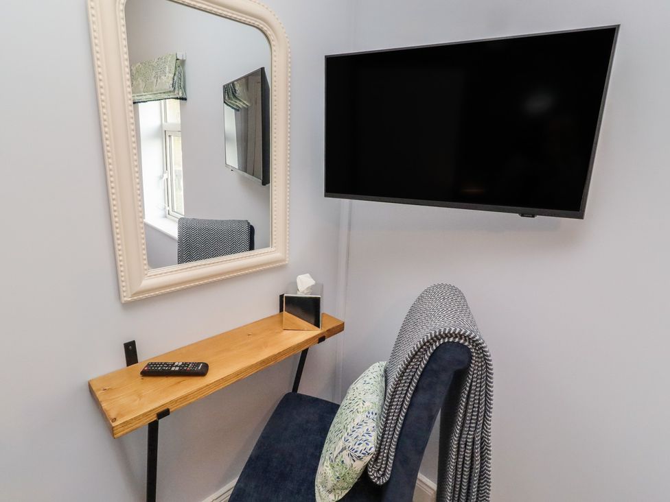 A small room with a mirror, chair and wall-mounted TV at Linn Cottage in Hexham