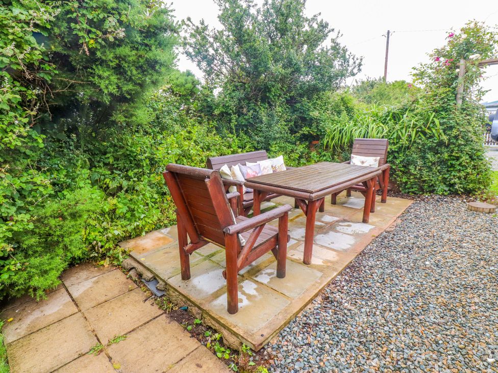 A garden with a stone patio and wooden furniture at 2 Llainwen Ty Croes