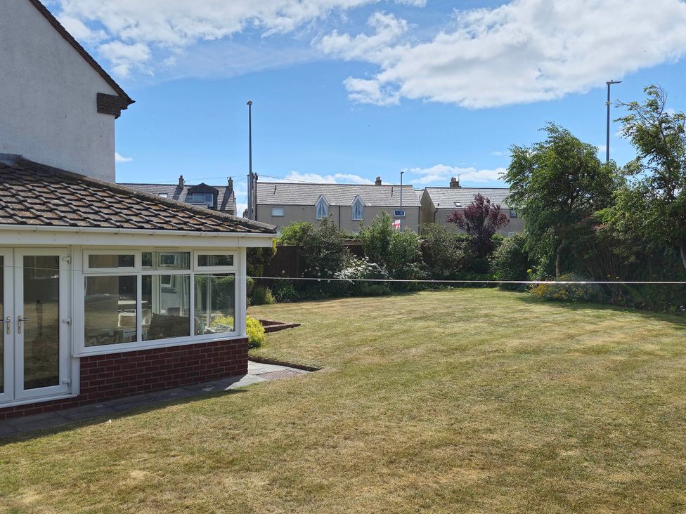 A garden with a conservatory and houses in the background at 13 Seafield Road