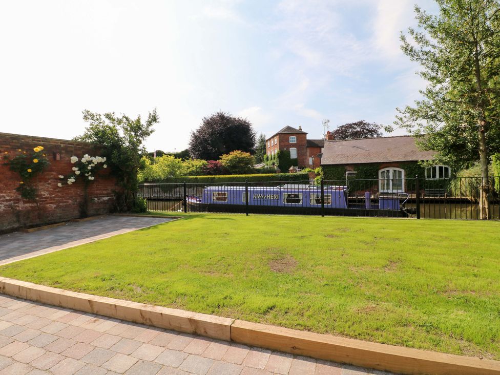 A garden with grass and a fence near a building at The Canalside Cottage in Derby