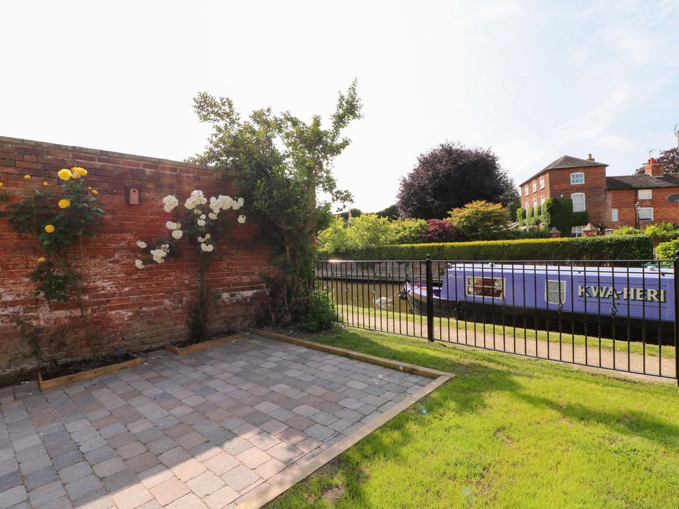 A garden with a brick wall, flowers, and a canal boat at The Canalside Cottage in Derby