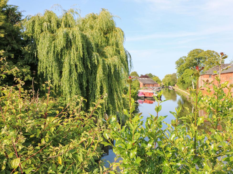 A canal with a willow tree and boathouses at The Canalside Cottage in Derby
