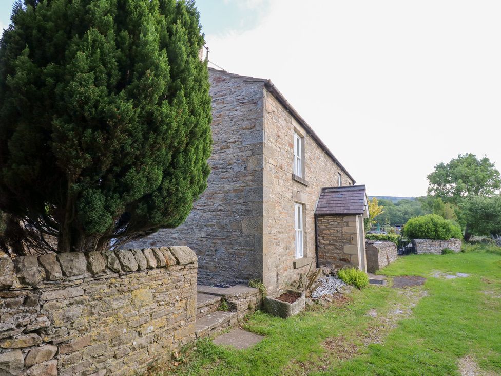 A house with a stone wall and a tree at Rosemary Cottage in Leyburn
