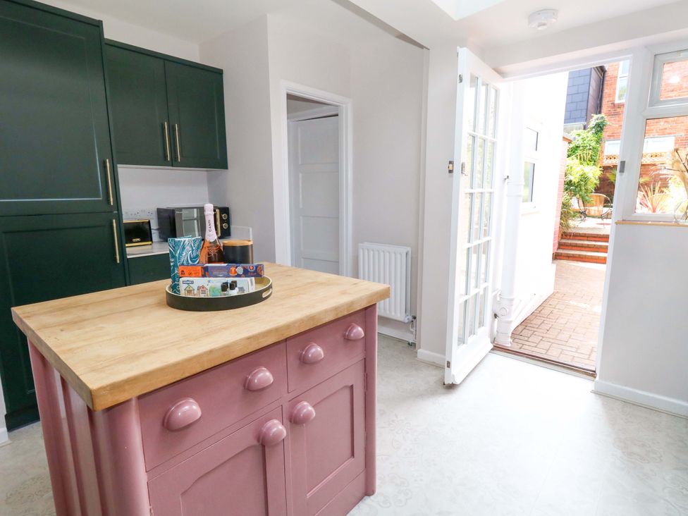 A kitchen with a pink island and dark green cabinets at Otter Cottage in Weymouth