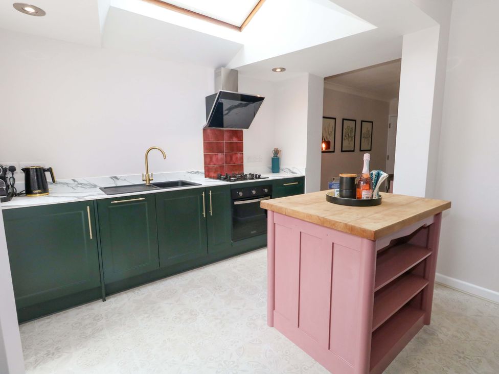 A kitchen with a pink island and green cabinets at Otter Cottage in Weymouth