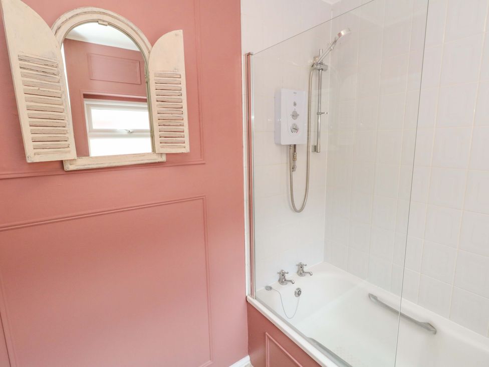 A bathroom featuring a bath tub with shower and a mirror at Otter Cottage in Weymouth