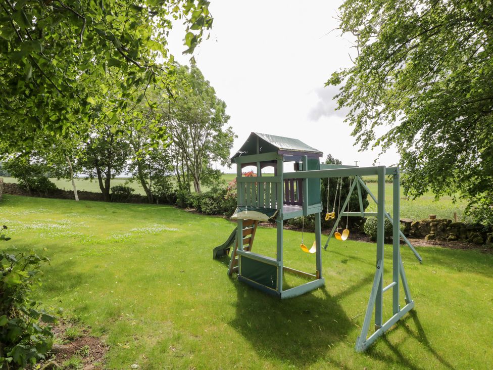 A garden with a playhouse and swing set at Marshill Farm house in Lanark