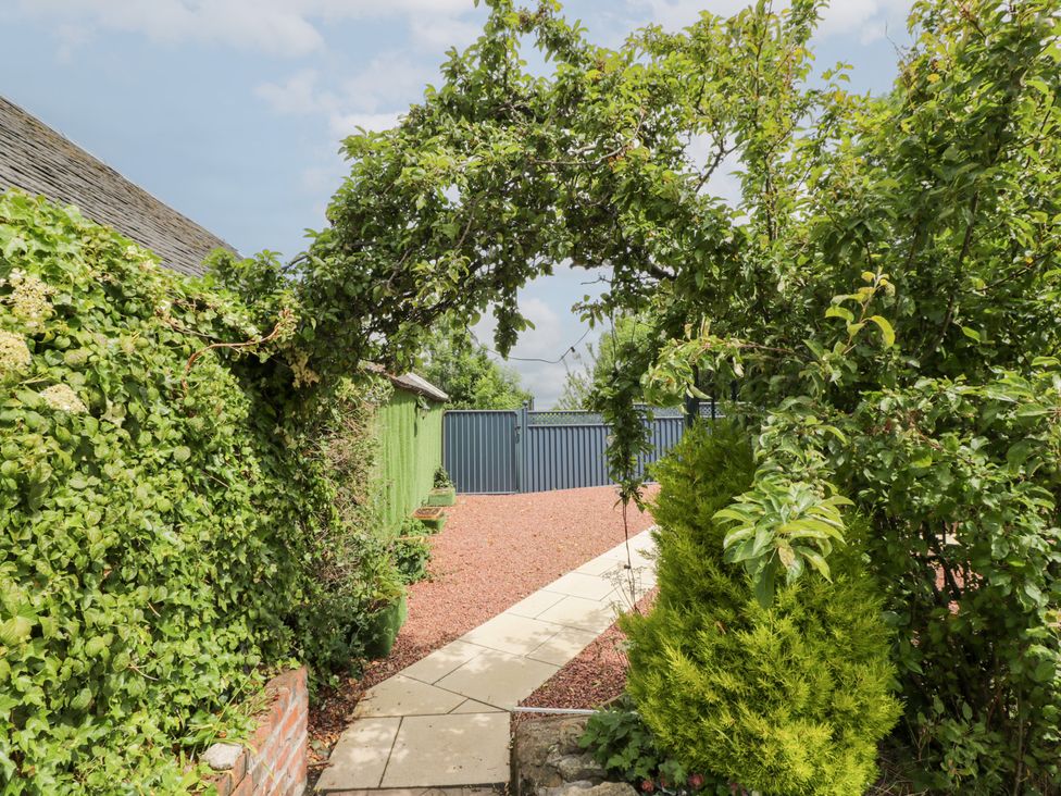 An archway with greenery leading to a gravel path and blue gates at Marshill Farm house in Lanark