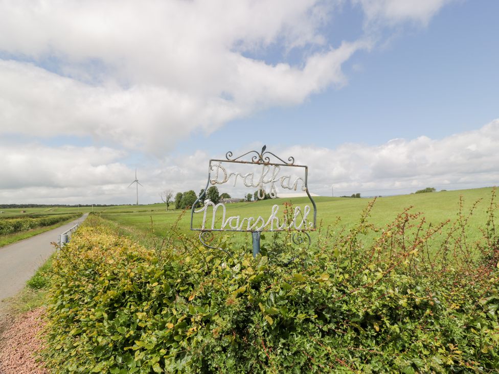 A sign for Draffan Marshill with a field and wind turbine in the background at Marshill Farm house in Lanark