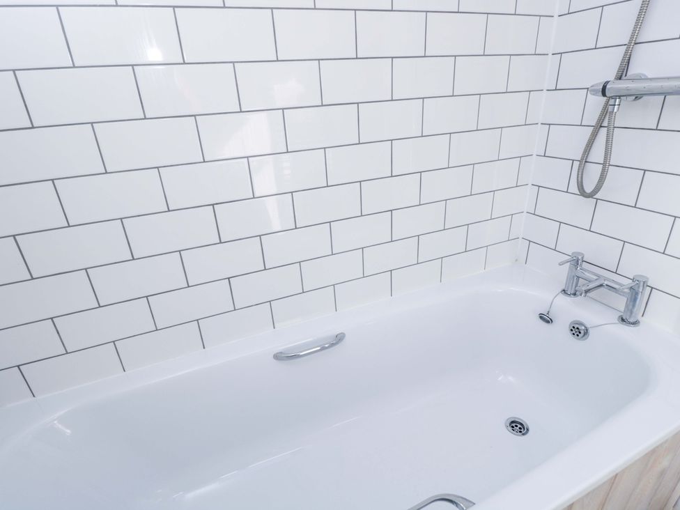 A bathtub with tiles on the wall at Barn Cottage in Frome