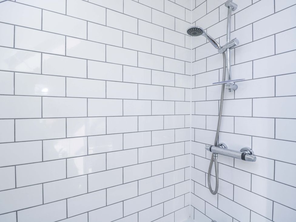 A bathroom with a showerhead and wall tiles at Barn Cottage in Frome